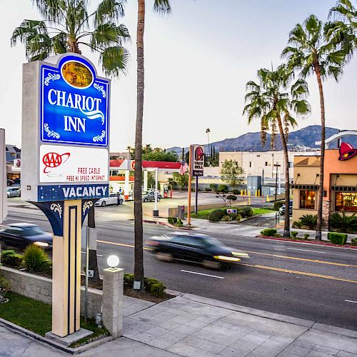 A roadside view featuring a Chariot Inn sign with vacancy status, palm trees, a few passing cars, and a Taco Bell in the background.