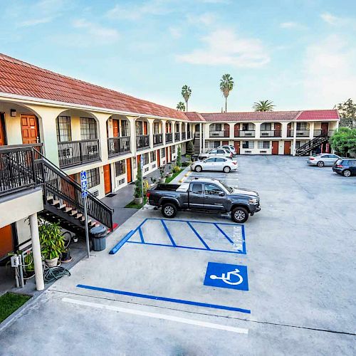 The image shows a two-story motel with a parking lot, accessible parking spaces, and several cars parked in front of the rooms.