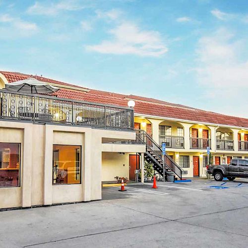 This image shows a two-story motel with a parking lot in front, featuring several vehicles and outdoor staircases for access.