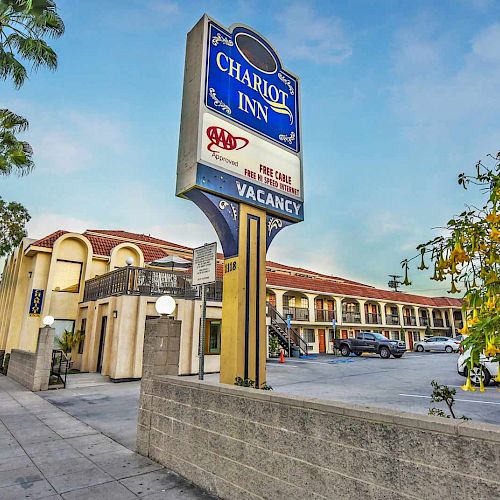 The image shows the exterior of Chariot Inn, a motel with a large sign indicating AAA approval, free Wi-Fi, and vacancy.