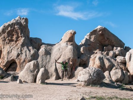 A person standing in front of large rock formations under a blue sky with a few scattered clouds.