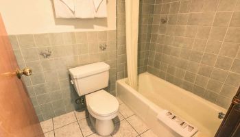 This image shows a bathroom with a toilet, a bathtub with a shower curtain, light blue tiles, and two towels folded over a towel rack above the toilet.