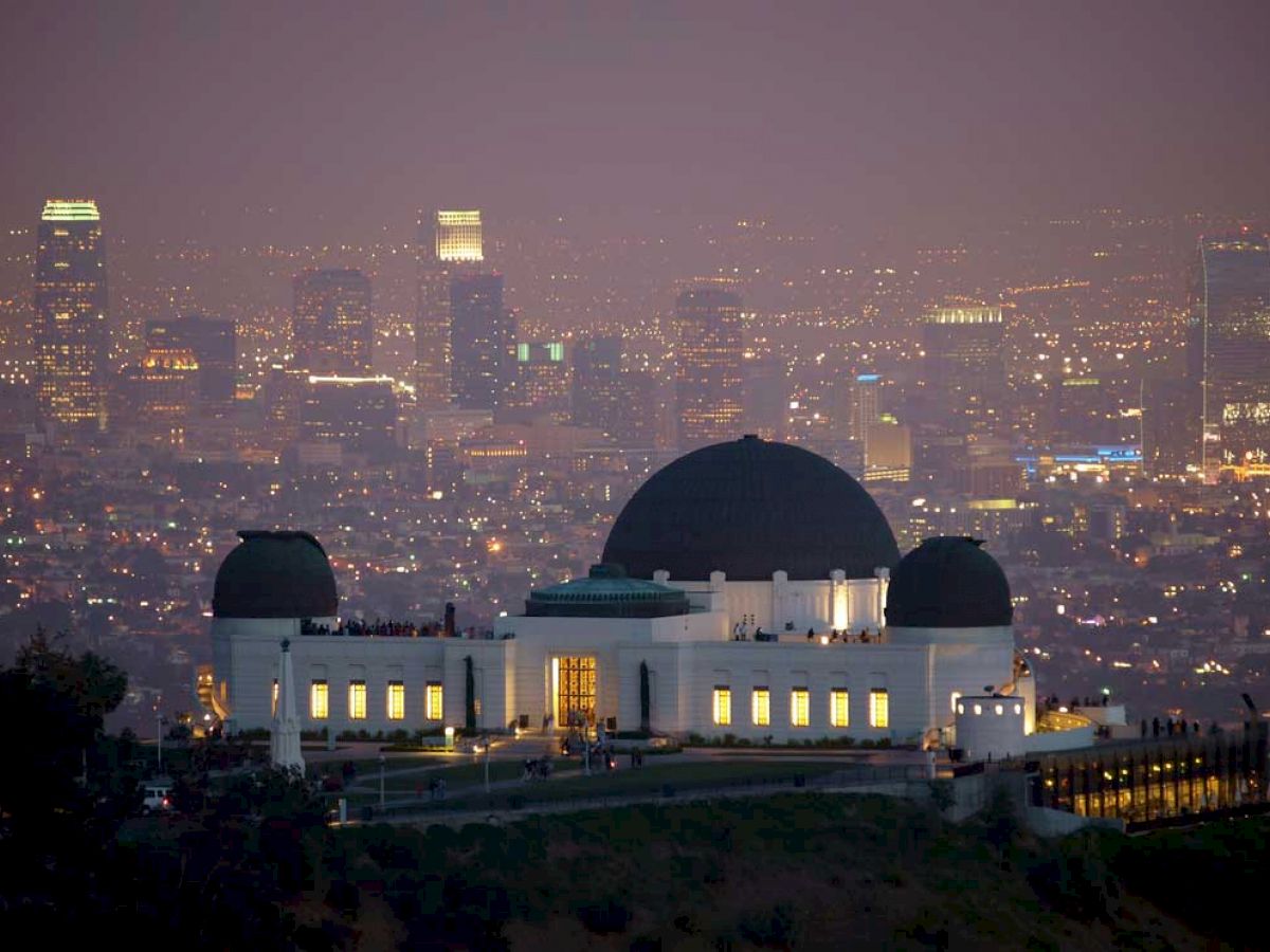 This image shows the Griffith Observatory in Los Angeles, with the city skyline illuminated in the background during the evening.